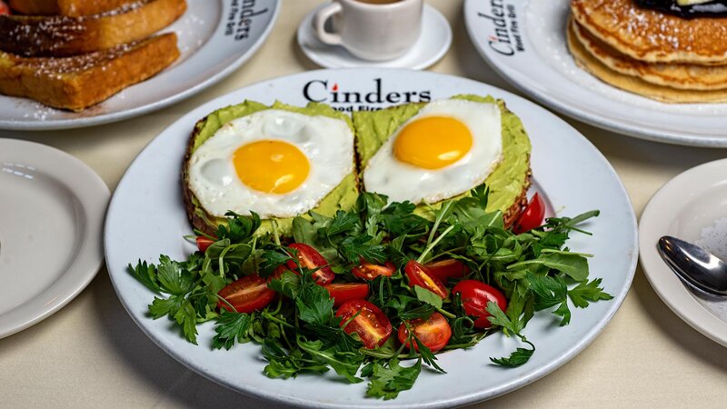 Avocado toast topped with fried eggs with side salad